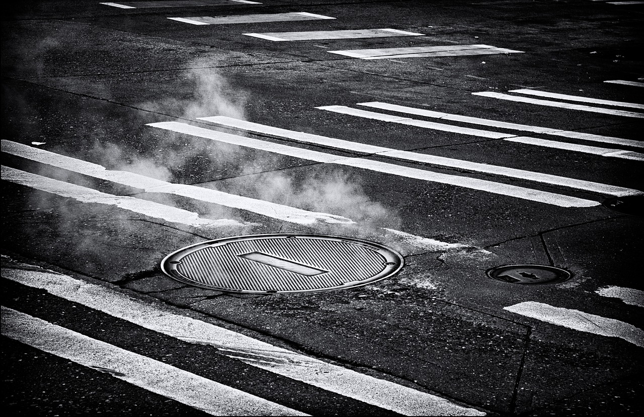 Black and white image of a cracked road with smoke rising from the fissure, illustrating damage and underground heat effects.