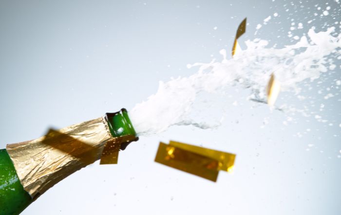 A champagne bottle popping open with bubbles and foam spilling out, symbolizing celebration and brand impact.